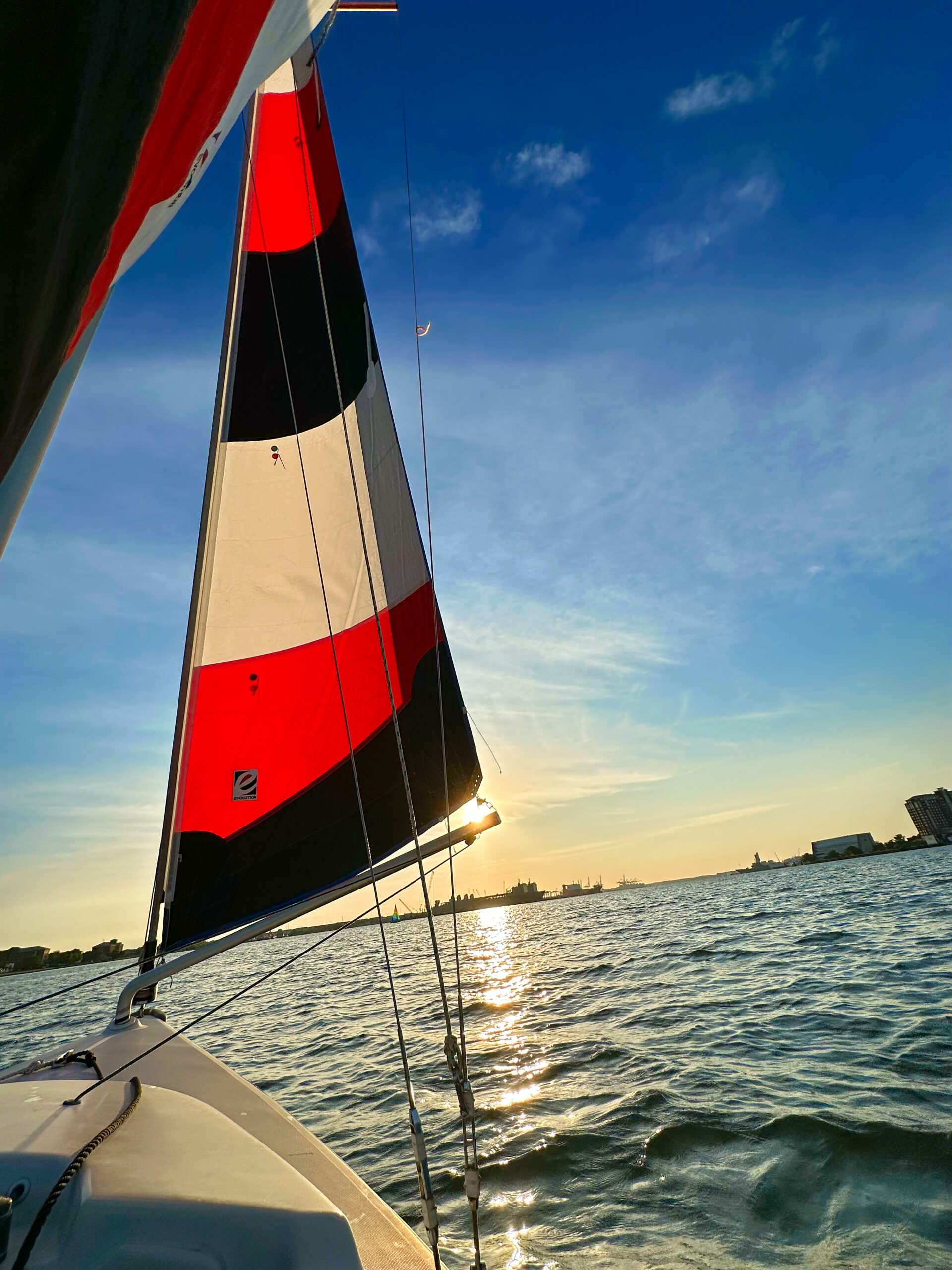 a sail boat at sunset with a red, white, and black sail.